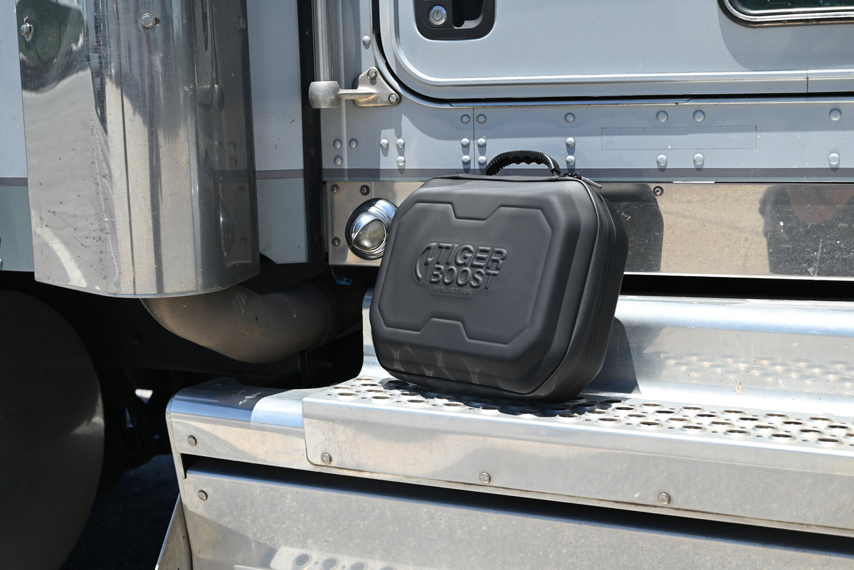 A black Tiger Boost hard shell protective case resting on the step of a silver truck.